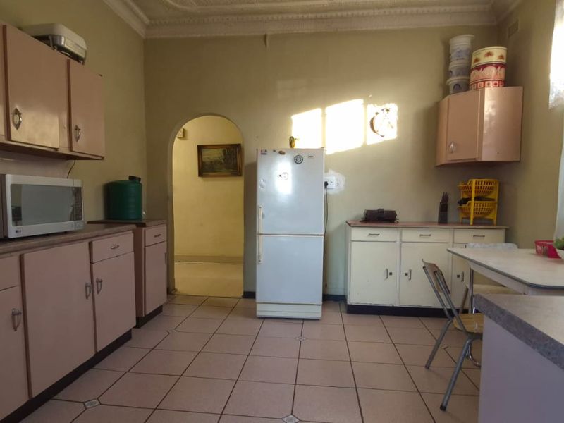 A dated kitchen featuring original cabinetry, tiled flooring, and a classic archway leading to the adjacent living space.