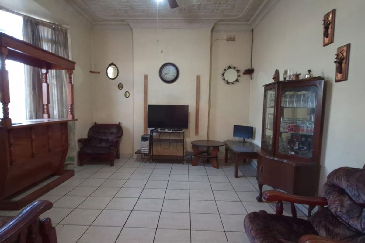 A living room featuring tiled flooring and ornate ceiling detailing, offering a dated interior space with potential for modernization.