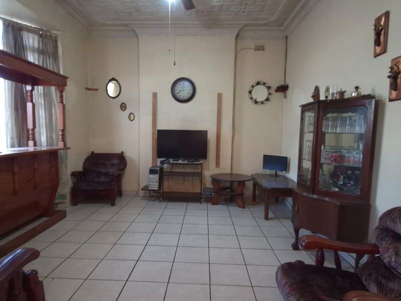 A living room featuring tiled flooring and ornate ceiling detailing, offering a dated interior space with potential for modernization.