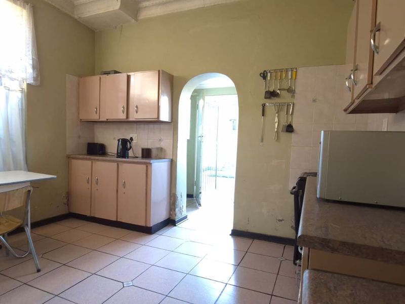 A dated kitchen featuring built-in cabinetry, tiled flooring, and a tiled backsplash, with visible wear on the lower wall surfaces.