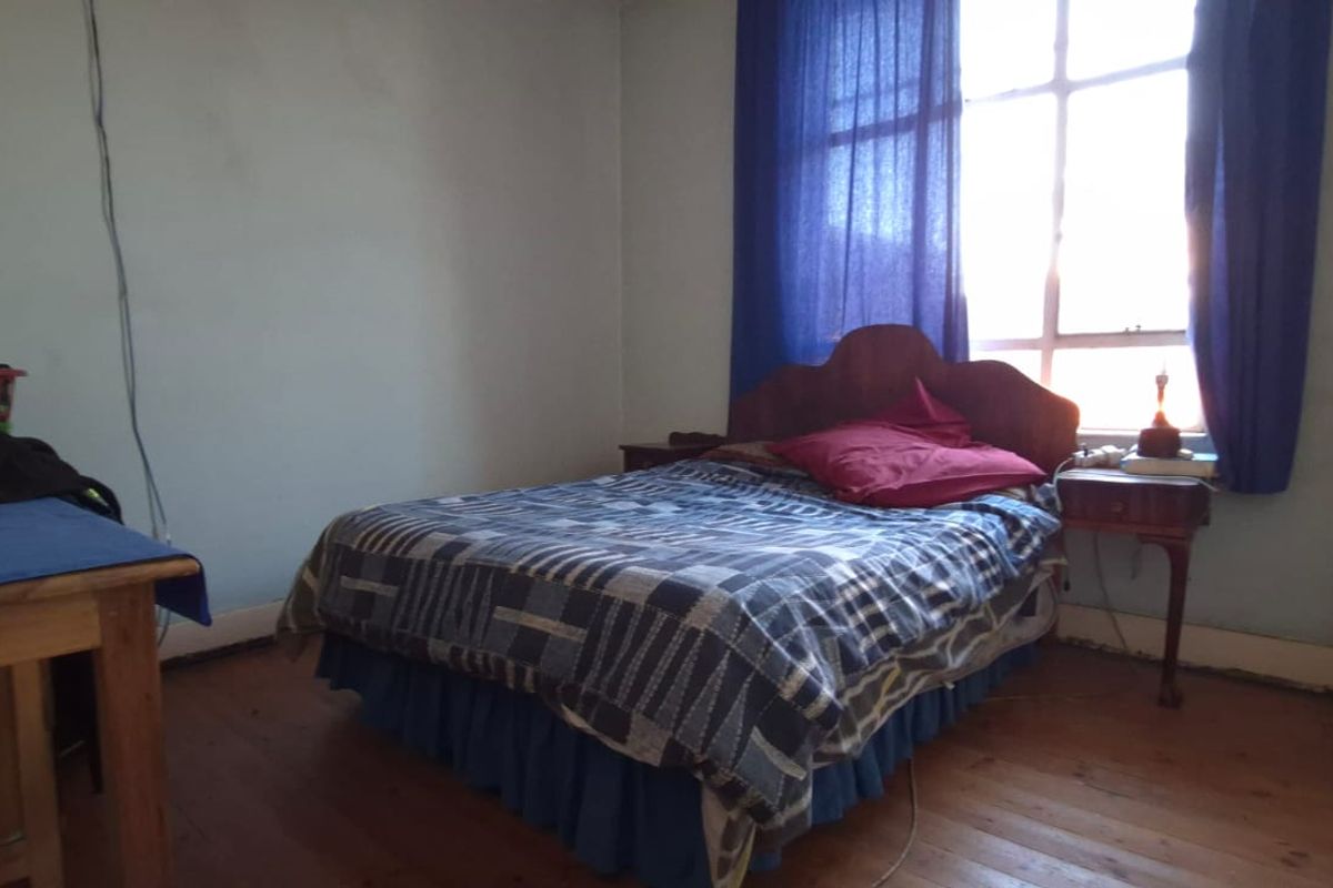 A bedroom featuring timber flooring and a large window, providing natural light. The space requires cosmetic updates to the walls and finishes.