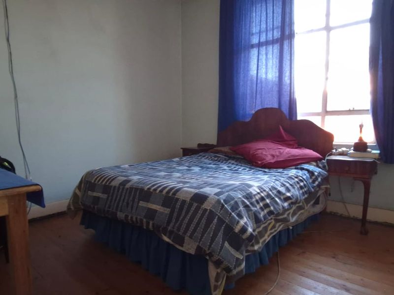 A bedroom featuring timber flooring and a large window, providing natural light. The space requires cosmetic updates to the walls and finishes.