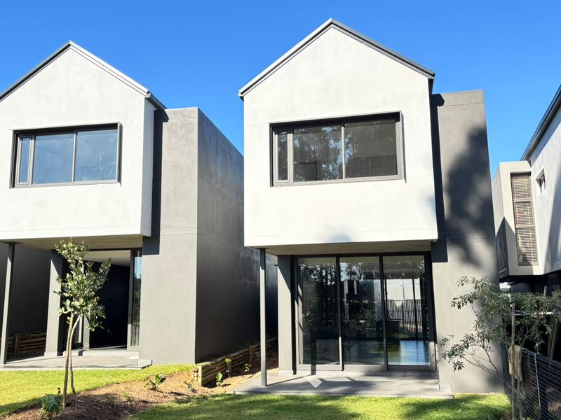 Rear view of modern two-story residential units featuring clean architectural lines, sliding glass doors, and private patio areas overlooking a landscaped lawn.