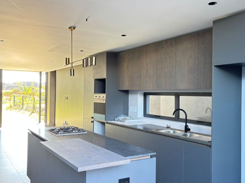 Modern open-plan kitchen featuring sleek dark cabinetry, stone countertops, a central island with a gas hob, and integrated appliances.