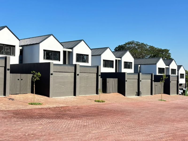 A row of modern townhouses featuring contemporary architectural design, dark garage doors, and a clean paved driveway area.