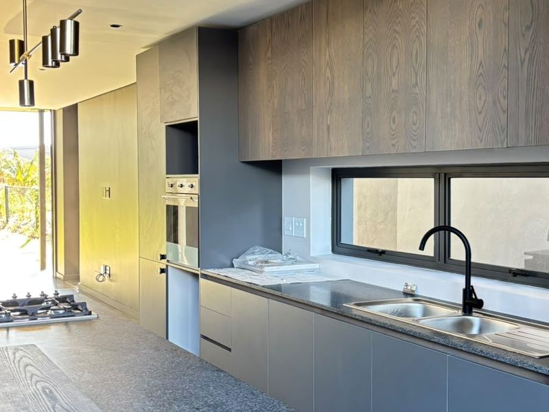 Modern kitchen featuring sleek cabinetry, stone countertops, built-in oven, gas hob, and high-quality finishes in an open-plan layout.