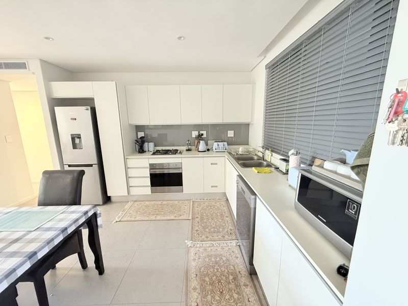 Modern kitchen featuring white cabinetry, stone countertops, integrated appliances, gas hob, and large windows with venetian blinds, offering a clean and functional workspace.