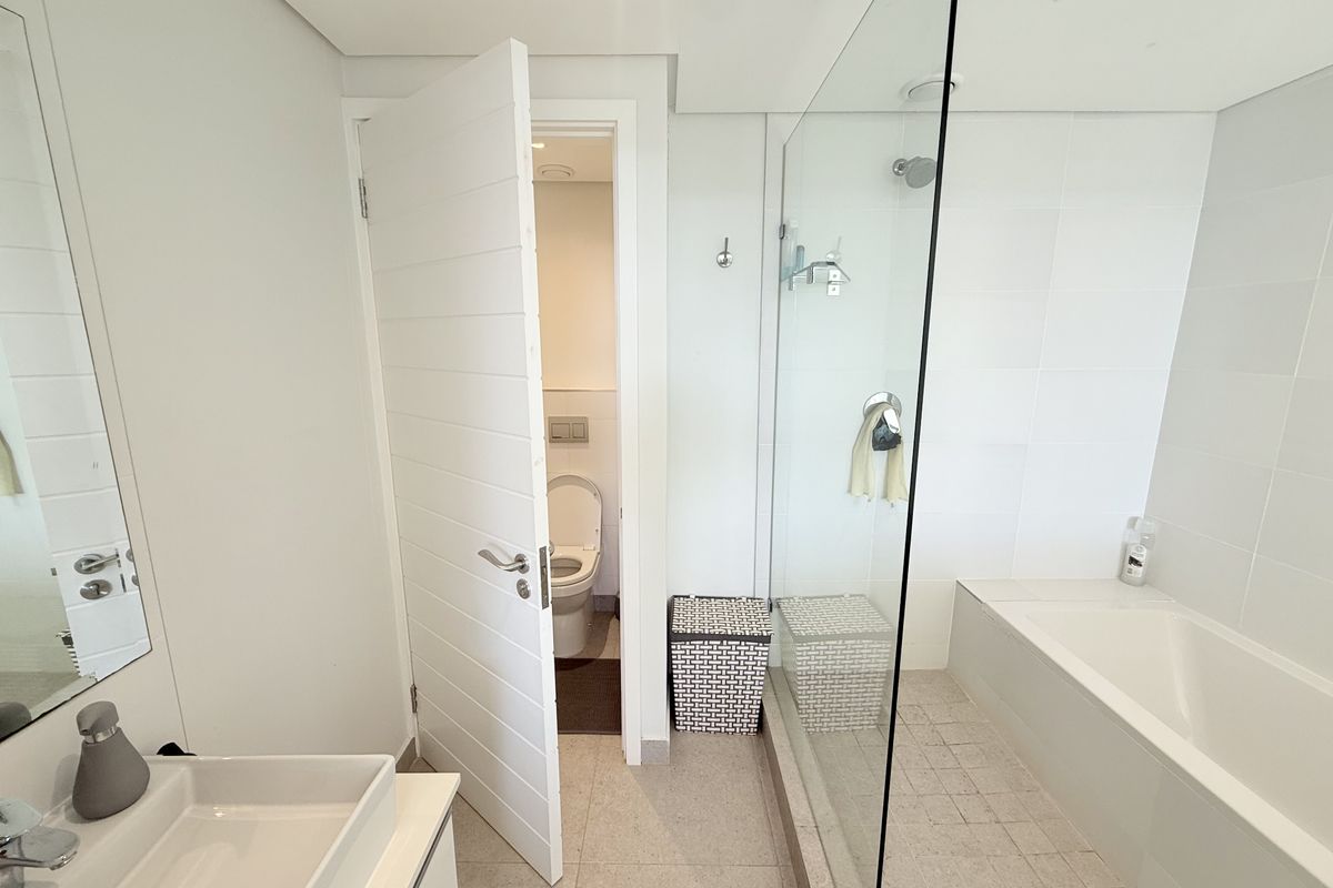 Modern bathroom featuring a vanity basin, glass-enclosed shower, built-in bathtub, and a separate toilet area with clean white finishes.