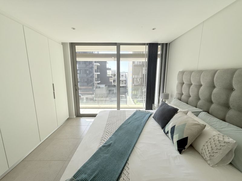 Modern bedroom featuring built-in cupboards, tiled flooring, and a large sliding glass door providing access to an outdoor balcony area.