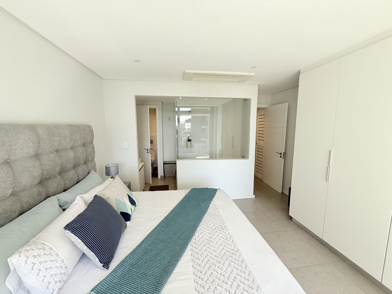Modern bedroom featuring built-in cupboards, tiled flooring, ducted air conditioning, and an en-suite bathroom with a contemporary glass partition wall.