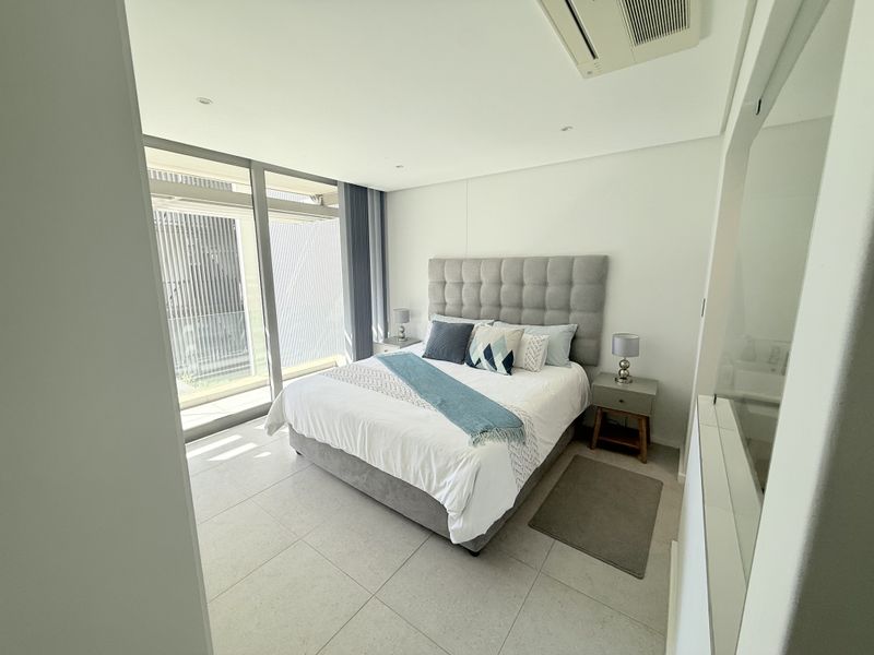 Modern bedroom featuring large floor-to-ceiling sliding glass doors, neutral tiled flooring, and integrated ducted air conditioning.