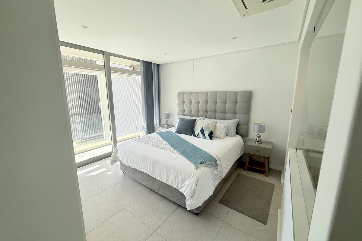 Modern bedroom featuring large floor-to-ceiling sliding glass doors, neutral tiled flooring, and integrated ducted air conditioning.