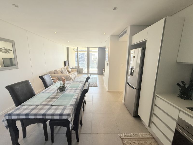 Modern open-plan living and dining area featuring sleek built-in cabinetry, tiled flooring, and seamless access to a private balcony through sliding glass doors.
