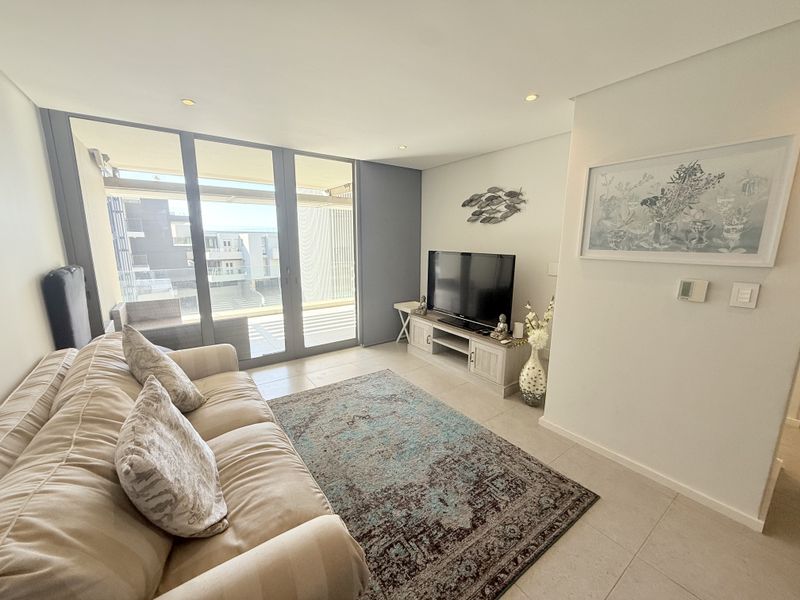 A bright and modern living room featuring tiled floors, recessed lighting, and large sliding glass doors that open onto a private balcony.
