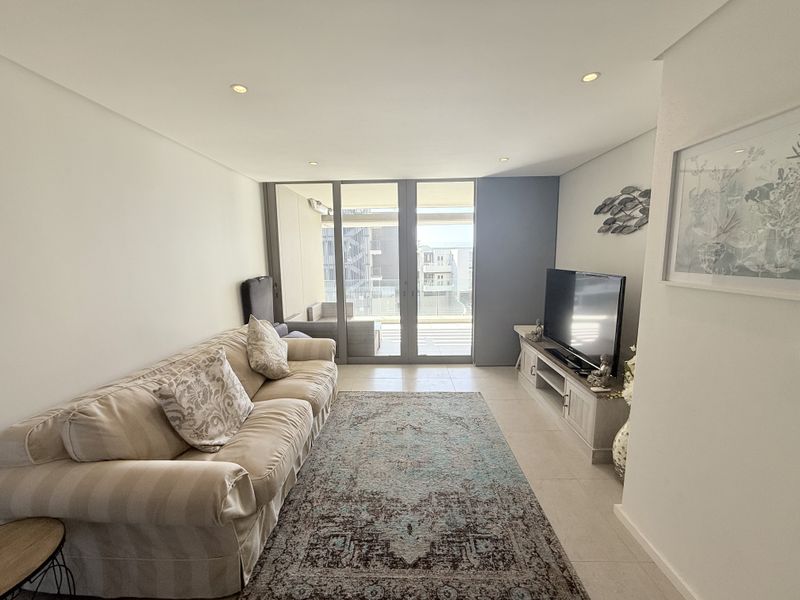 A bright living room featuring tiled flooring, recessed downlighting, and large sliding glass doors providing access to an outdoor balcony area.