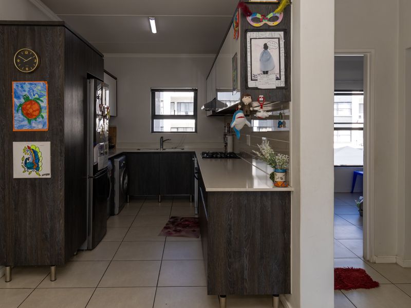 A functional kitchen featuring dark wood-grain cabinetry, stone countertops, a gas hob, and tiled flooring, providing a practical workspace with integrated storage.
