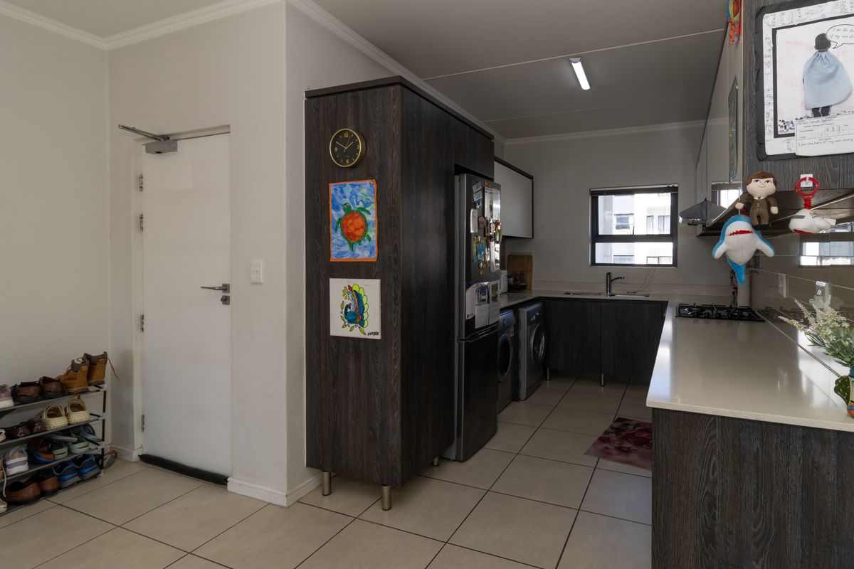 Modern kitchen featuring dark wood cabinetry, stone countertops, integrated gas hob, extractor fan, and dedicated space for laundry appliances.
