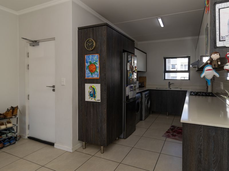 Modern kitchen featuring dark wood cabinetry, stone countertops, integrated gas hob, extractor fan, and dedicated space for laundry appliances.