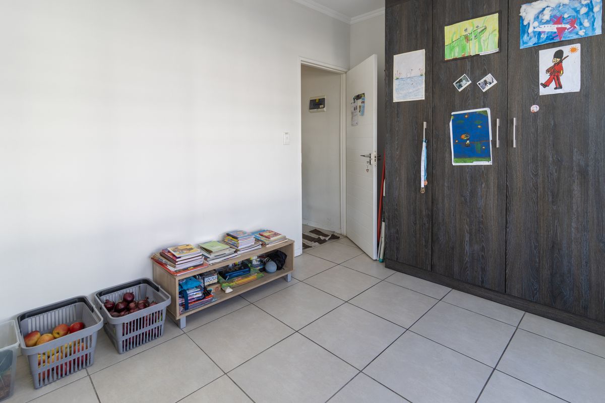 A bedroom featuring dark wood-finish built-in cupboards and neutral floor tiles, offering a clean and functional space.