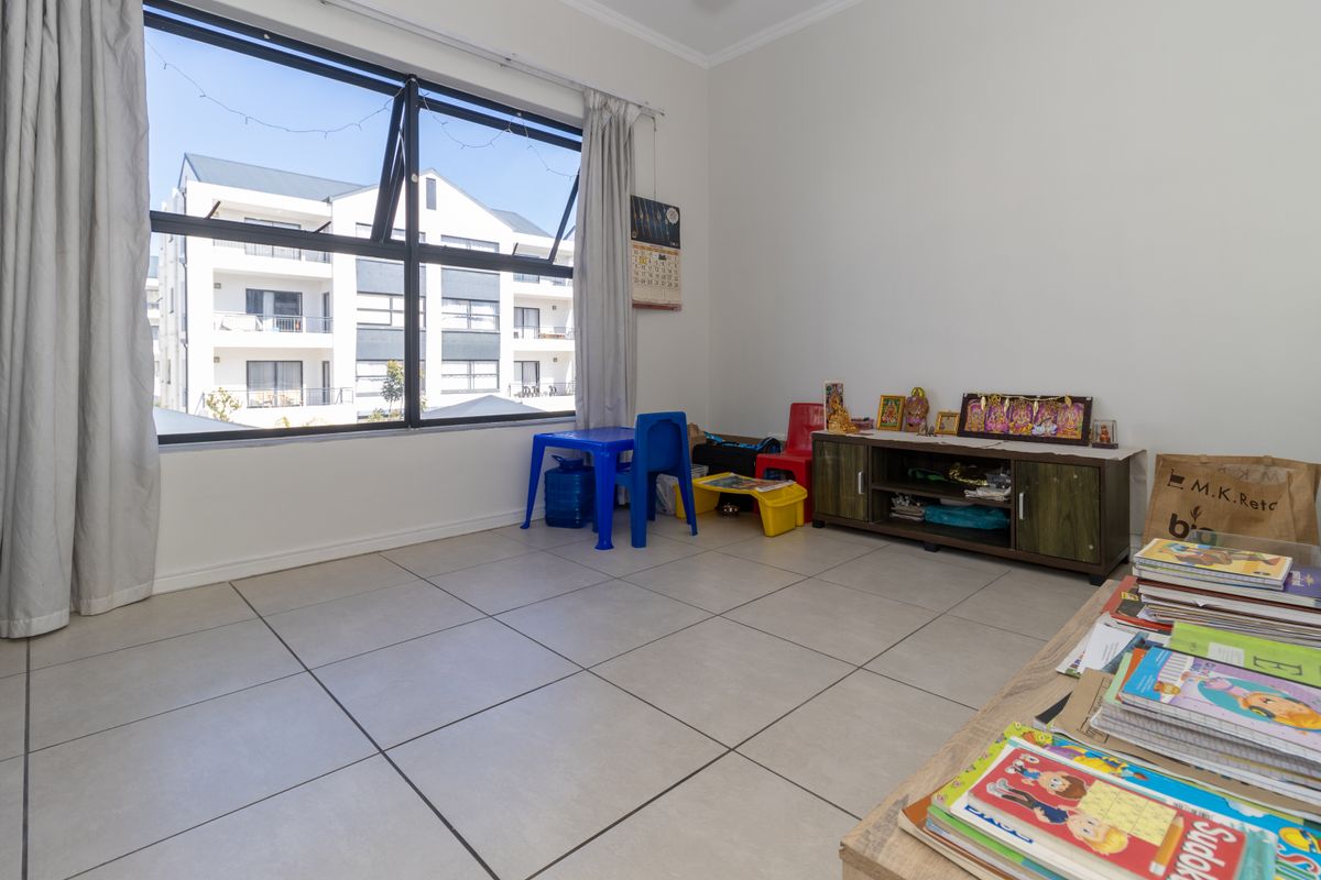 A bright living area featuring large aluminium windows and neutral tiled flooring, offering a versatile space for relaxation or family activities.