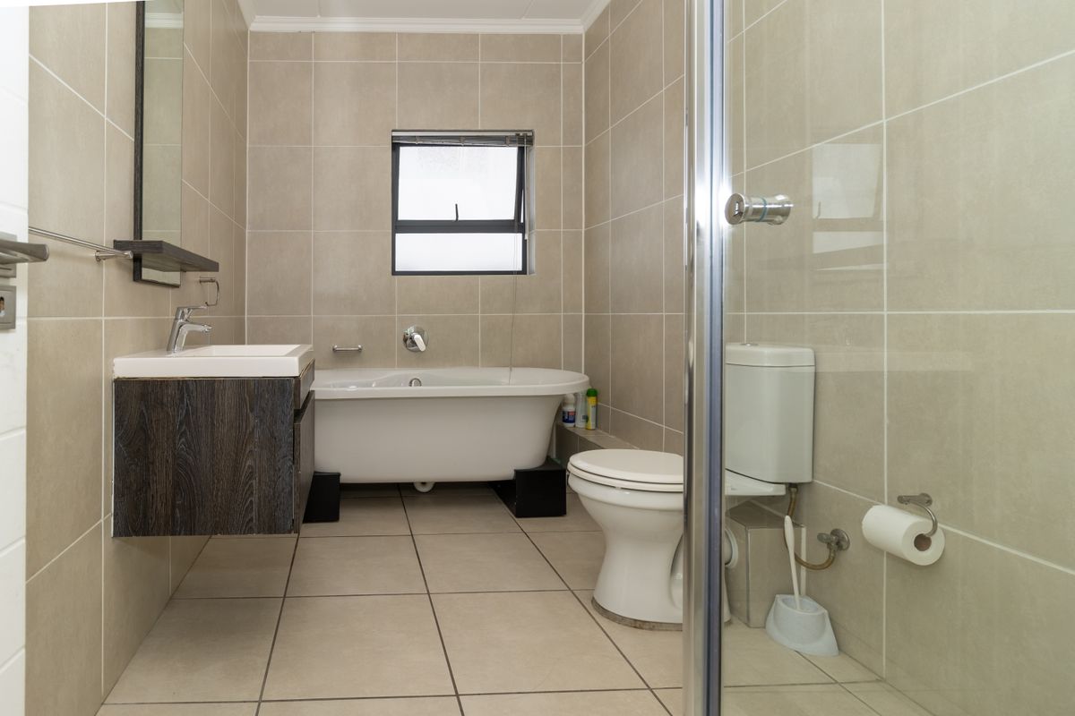 A modern bathroom featuring a freestanding bathtub, wall-mounted vanity, toilet, and a glass-enclosed shower with neutral floor-to-ceiling tiling.