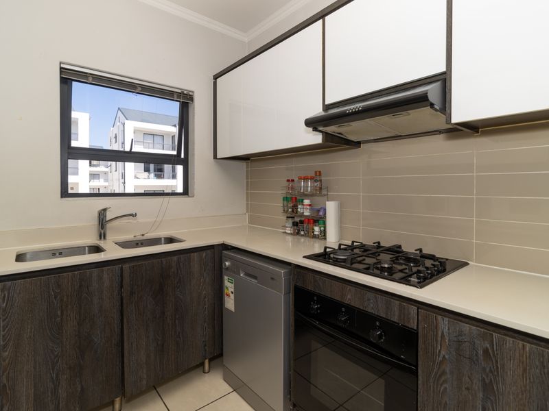 Modern kitchen featuring dark wood-grain cabinetry, stone countertops, a gas hob, built-in oven, and a double basin sink with a tiled backsplash.