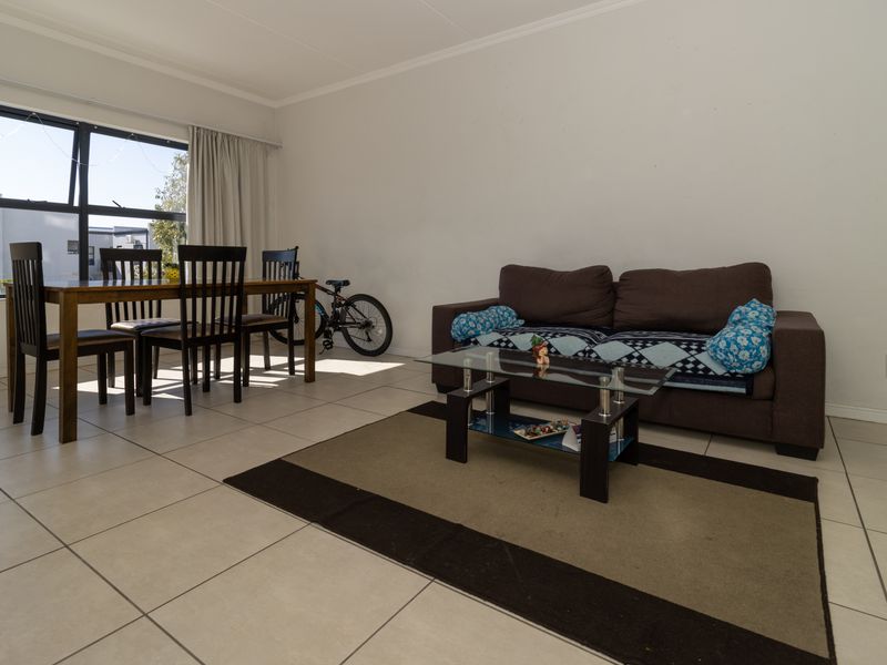 Open-plan living and dining area featuring neutral tiled flooring, coved ceilings, and large aluminium-framed windows providing natural light.