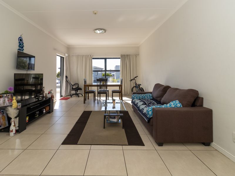 Open-plan living and dining area featuring neutral tiled flooring, large windows for natural light, and direct access to an outdoor balcony.