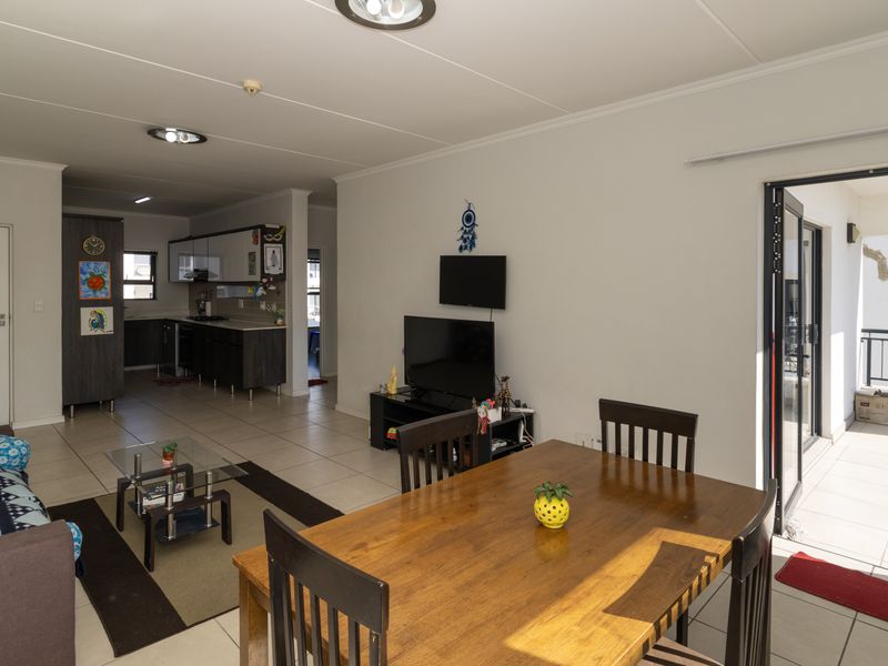 Open-plan living and dining area featuring tiled floors, recessed lighting, and a modern kitchen, with direct access to a private balcony.