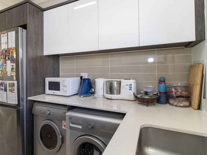 A functional laundry area featuring modern white and dark wood cabinetry, stone countertops, a stainless steel sink, and dedicated space for laundry appliances.