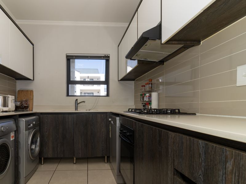 Modern kitchen featuring dark wood-grain lower cabinets, white upper cabinets, stone countertops, gas hob, extractor fan, and integrated laundry appliance space.