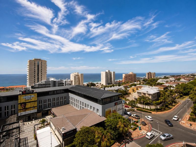 Elevated panoramic view overlooking the surrounding urban landscape, coastal buildings, and the ocean horizon under a clear blue sky.