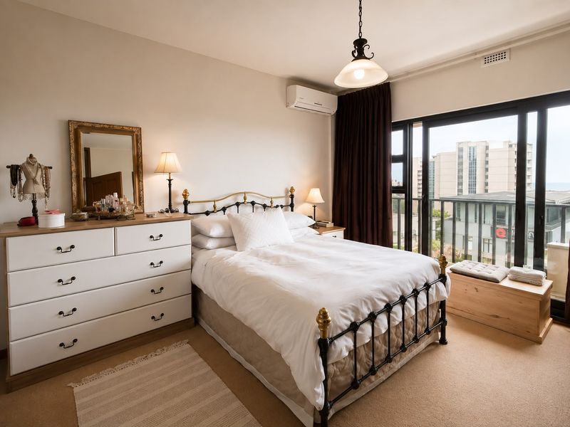 A well-maintained bedroom featuring carpet flooring, a split-system air conditioner, and large sliding glass doors providing access to a balcony with urban views.