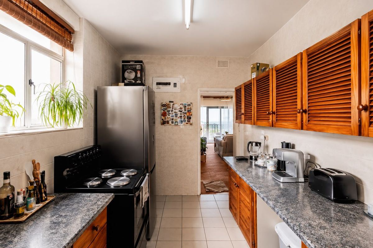 A functional kitchen featuring louvered wooden cabinetry, durable laminate countertops, and ceramic tiled flooring, offering a practical layout with direct access to the living area.