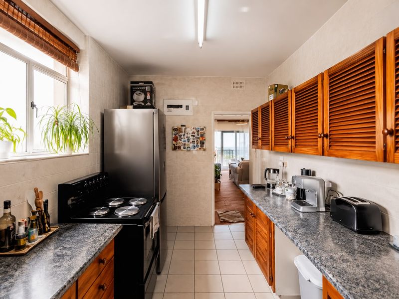 A functional kitchen featuring louvered wooden cabinetry, durable laminate countertops, and ceramic tiled flooring, offering a practical layout with direct access to the living area.