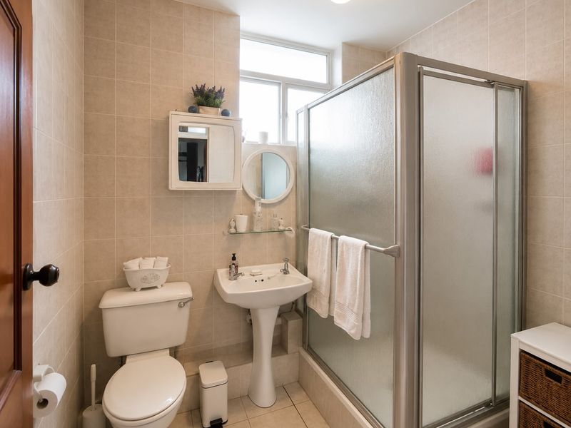 A functional bathroom featuring a pedestal sink, a shower enclosure with frosted glass doors, and neutral ceramic wall and floor tiling.