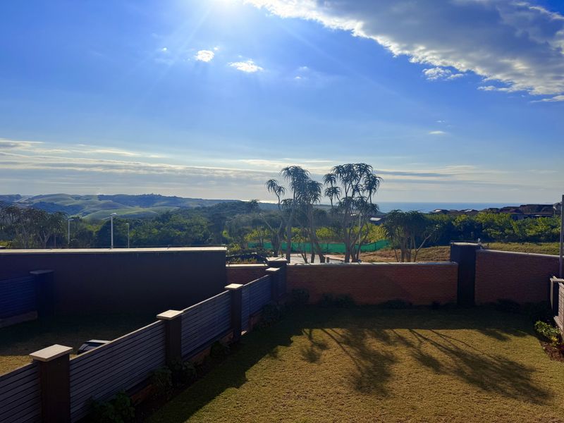 An elevated view overlooking a private garden with brick boundary walls and slatted fencing, featuring scenic coastal and landscape vistas.