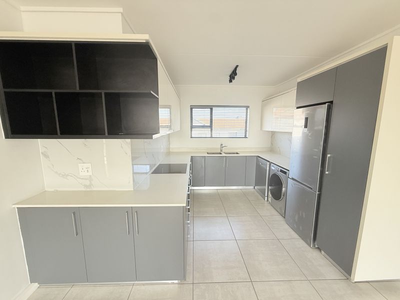 Modern, well-appointed kitchen featuring sleek grey and white cabinetry, stone countertops, marble-look splashbacks, and integrated appliances in a clean, contemporary layout.