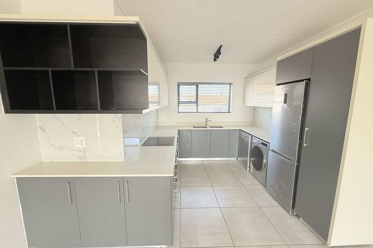 Modern, well-appointed kitchen featuring sleek grey and white cabinetry, stone countertops, marble-look splashbacks, and integrated appliances in a clean, contemporary layout.