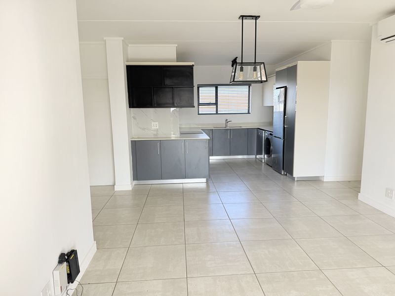 Modern open-plan kitchen featuring sleek grey and black cabinetry, marble-look splashback, tiled flooring, and integrated lighting in a spacious, well-lit living area.