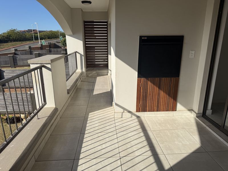 A covered balcony featuring tiled flooring, a built-in braai, and a metal balustrade, offering a functional outdoor entertainment space.