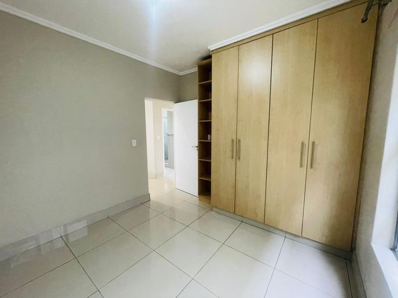 A bright, empty bedroom featuring neutral tiled flooring and extensive built-in wooden cupboards with integrated shelving.