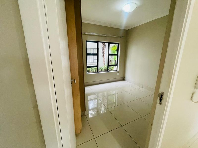 A bright, empty bedroom featuring neutral tiled flooring, a built-in cupboard, and a window providing natural light.
