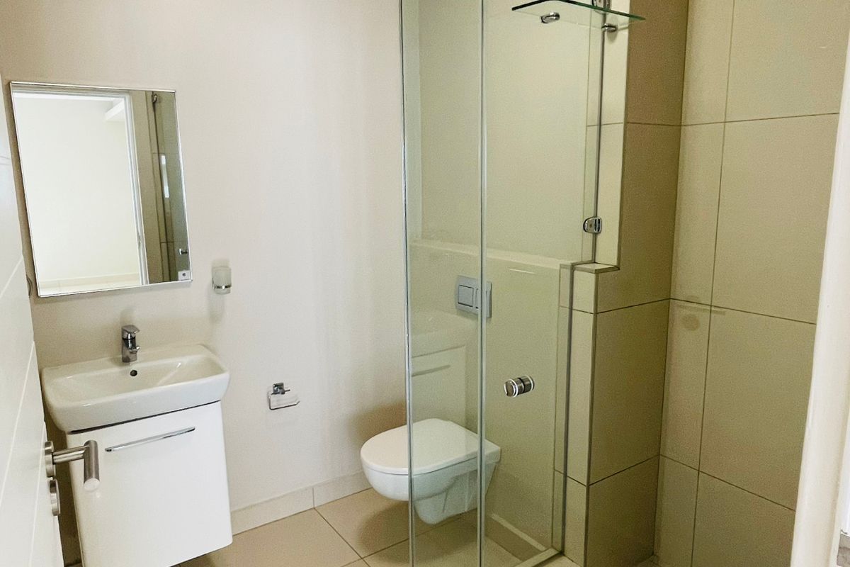Modern bathroom featuring a wall-mounted vanity, glass shower enclosure, and wall-mounted toilet with neutral floor-to-ceiling tiling.