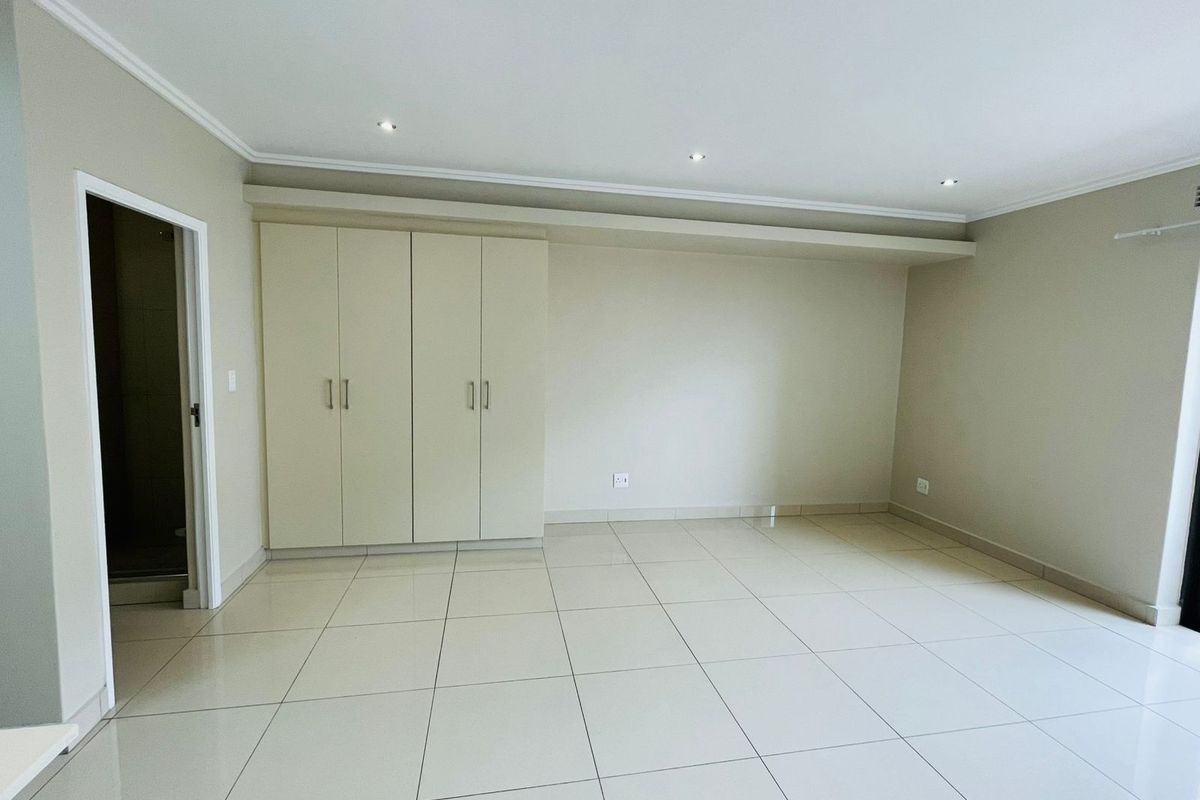 A spacious, empty bedroom featuring neutral tiled flooring, built-in cupboards, and recessed downlighting, offering a clean and versatile living space.