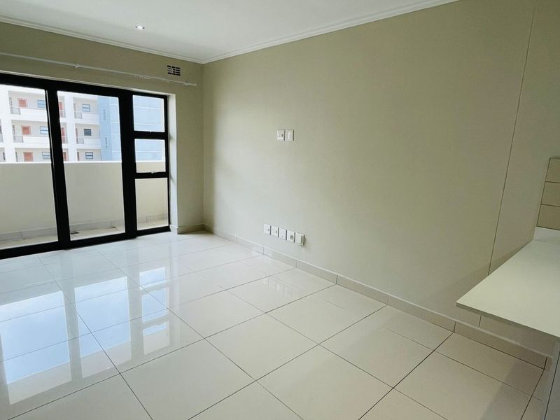 A bright, empty living area featuring polished porcelain floor tiles, recessed lighting, and a sliding glass door leading to a balcony.