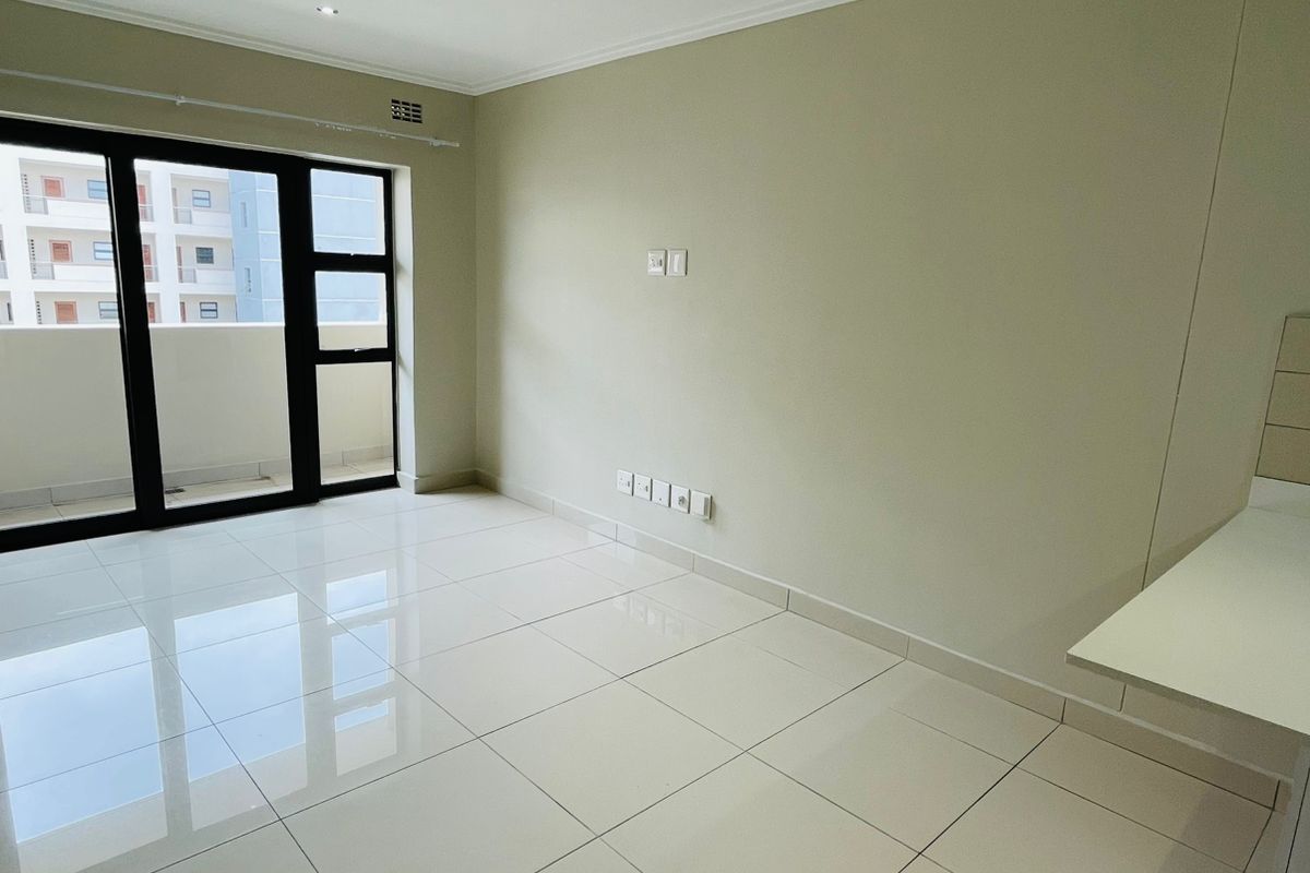 A bright, empty living area featuring polished porcelain floor tiles, recessed lighting, and a sliding glass door leading to a balcony.