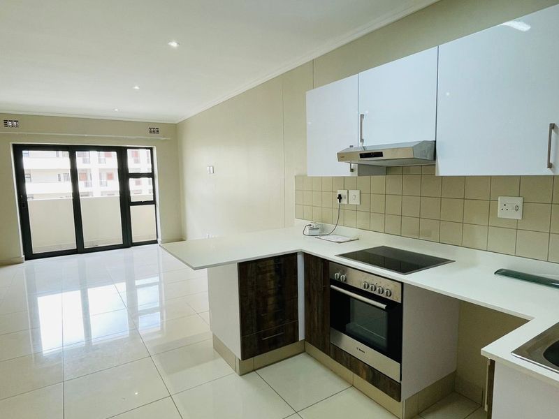 Modern open-plan kitchen and living area featuring sleek cabinetry, integrated appliances, tiled flooring, and large sliding doors leading to a balcony.