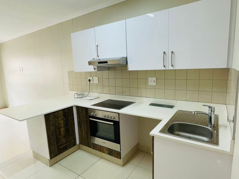 Modern kitchen featuring white and wood-finish cabinetry, integrated electric hob and oven, stainless steel sink, and neutral tiled flooring.