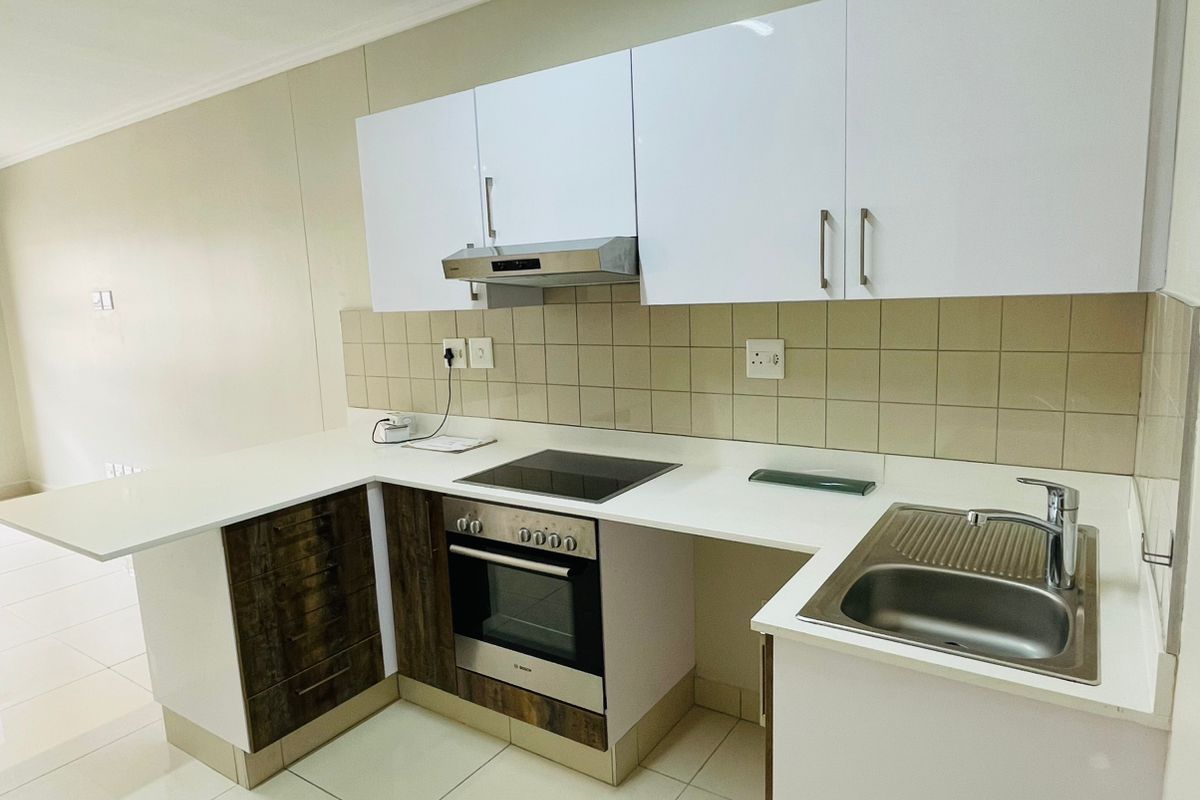 Modern kitchen featuring white and wood-finish cabinetry, integrated electric hob and oven, stainless steel sink, and neutral tiled flooring.